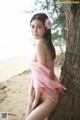 A woman in a pink dress leaning against a tree on the beach.