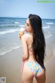 A woman in a bikini eating an ice cream cone on the beach.