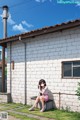 A girl sitting on a bench in front of a white brick building.